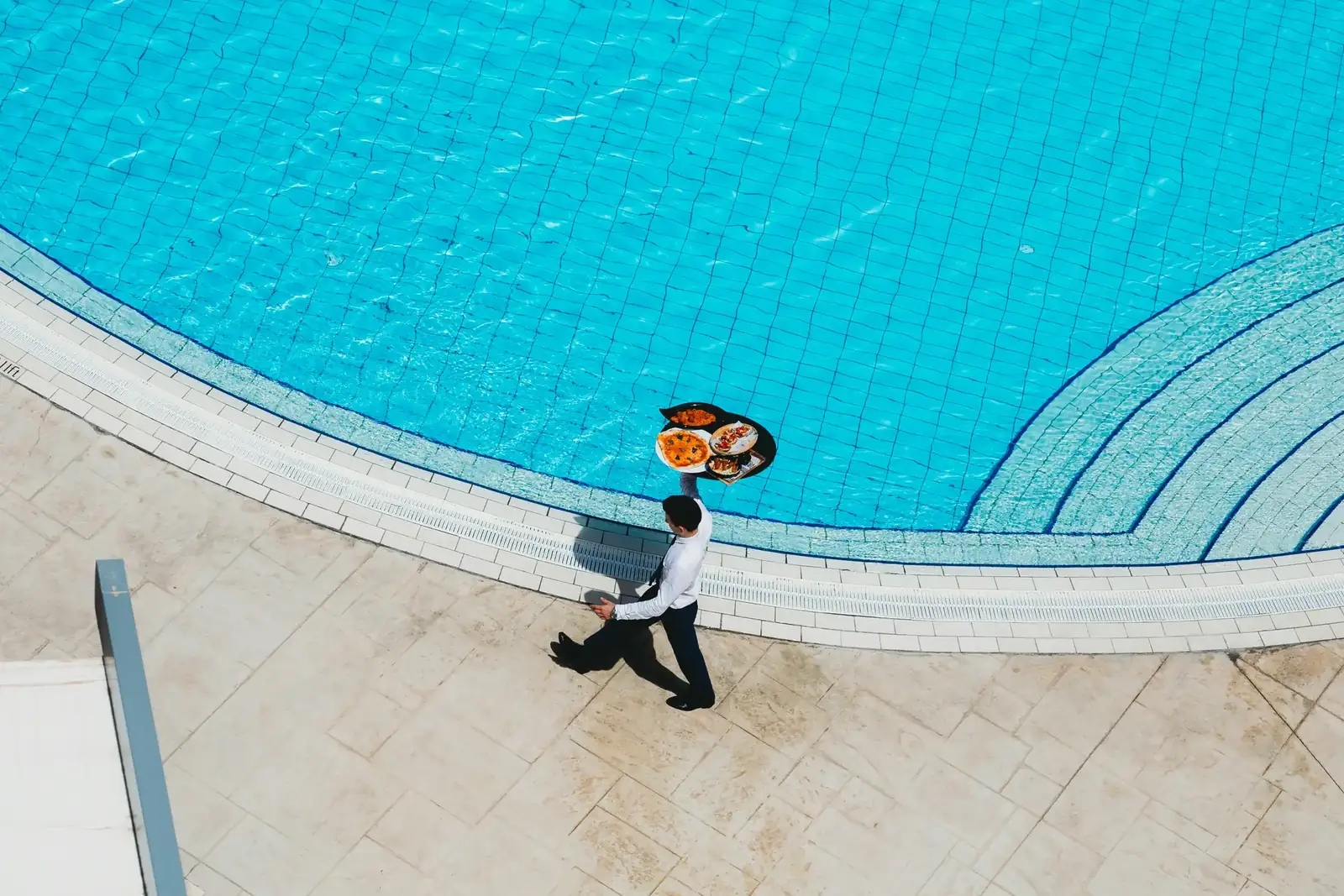 Vista aérea de garçom servindo à beira da piscina de um hotel
